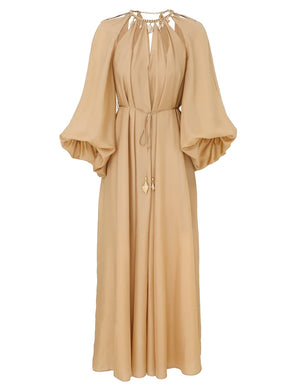 The Mahon Maxi Dress by Zimmermann is a long beige dress with billowy sleeves, a gathered neckline, and a gold-accented tie waist.