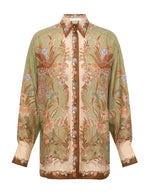 The Indra Relaxed Shirt by Zimmermann is a long-sleeved silk shirt with a green and beige base, earthy floral-bird print, and patterned collar and cuffs.
