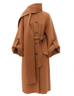 The Valiant Wool Scarf Coat by Zimmermann is a camel design with large buttons, a matching belt, wide sleeves, and a scarf draped at the collar.
