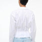 Person stands with their back to the camera, wearing the Staud Primrose Shirt—a white poplin button-down—paired with light blue jeans, set against a plain background.