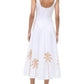 A person wearing the Staud Wells Palm Embroidery Dress—a sleeveless white cotton poplin dress with a fitted waist and tan palm tree embroidery near the hem—paired with heeled sandals.