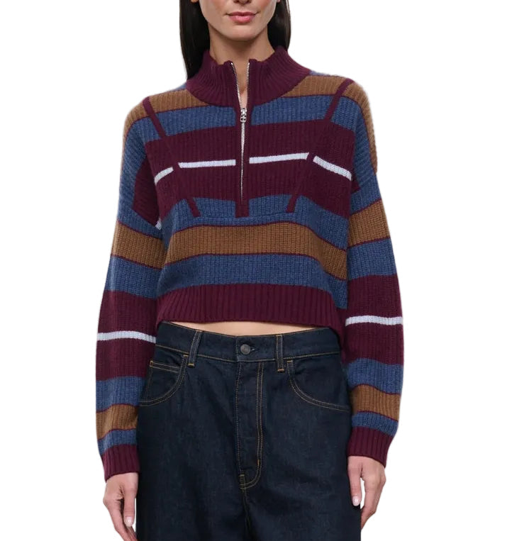 A woman wears the Staud Hampton Cashmere Sweater—a striped, cropped style featuring a half-zip collar in burgundy, blue, brown, and white—paired with high-waisted dark denim jeans.