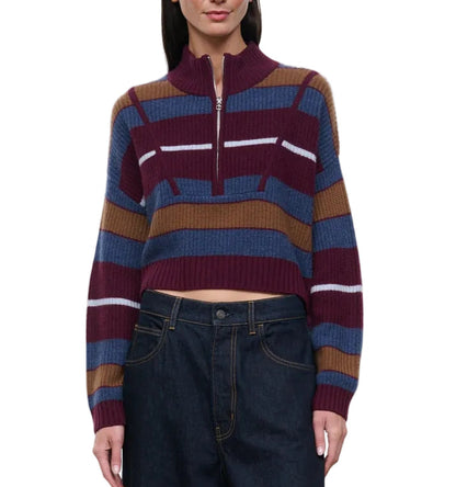 A woman wears the Staud Hampton Cashmere Sweater—a striped, cropped style featuring a half-zip collar in burgundy, blue, brown, and white—paired with high-waisted dark denim jeans.