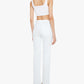A woman stands facing away, wearing Mother’s Kick It high-rise straight-leg jeans crafted from recycled stretch denim, a white crop top, and white heels against a plain white background.