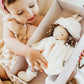 A young child holds the Bunnies By the Bay Glad Dreams Elsie Doll, a soft doll dressed in white with a matching coat and hat, inside a keepsake wardrobe box.