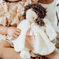 A child holds the soft Glad Dreams Elsie Doll by Bunnies By the Bay, dressed in a white coat and pink dress with brown yarn hair and embroidered features—perfect for gifting or storing in a keepsake box.