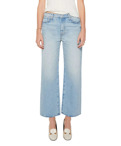 A person wearing The Dodger Flood slouchy light blue jeans by Mother with an oversized fit and white shoes, standing against a white background. Only the lower torso and legs are visible.