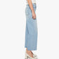 A person stands sideways against a plain background wearing The Dodger Flood wide-leg cropped jeans by Mother in light blue denim, paired with a white short-sleeve top and white heeled shoes.
