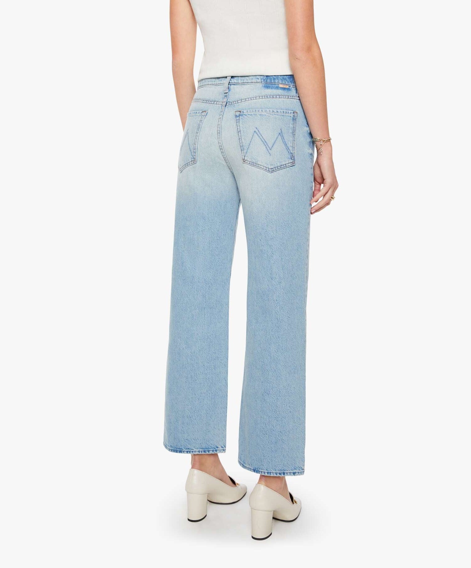 A person wearing The Dodger Flood slouchy, light blue denim jeans by Mother, styled with white heels and standing with their back to the camera against a plain white background.