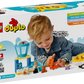 A child enjoys the LEGO® DUPLO® First Time at the Airport set by Legos - Toyhouse, which includes a plane, control tower, and figures. Designed for ages 2+, it offers educational value as a fun preschool learning toy.