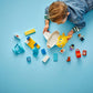 A young child in denim plays on a blue surface with colorful preschool toys, including building blocks, animal and vehicle figures, and the LEGO® DUPLO® First Time at the Airport set by Legos - Toyhouse.