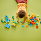 A child plays on a green floor with the LEGO® DUPLO® 3in1 Dinosaurs on Wheels set by Legos - Toyhouse, assembling colorful dinosaur pieces from this toddler building set.