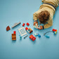 A child in beige clothes lies on a light blue floor, playing with the LEGO® DUPLO® McQueen's Visit to Doc's Garage set from Legos - Toyhouse.