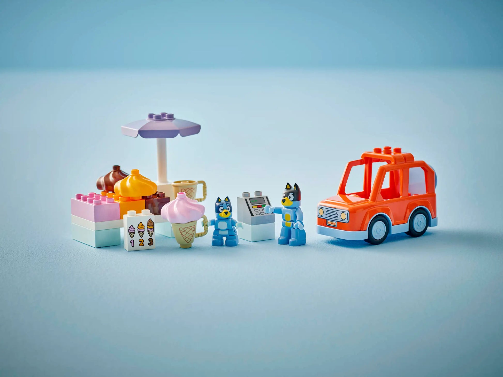 The LEGO® Ice Cream Trip with Bluey by Legos - Toyhouse includes an ice cream stand, desserts, two animal figures, a cash register, and an orange toy car—an ideal colorful toddler toy on a light blue background.