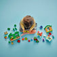 A child sits on a blue floor, playing with the LEGO® DUPLO® Grandpa Pig's Garden and Greenhouse building set from Legos - Toyhouse, arranging colorful blocks and Peppa Pig figures in front of them.
