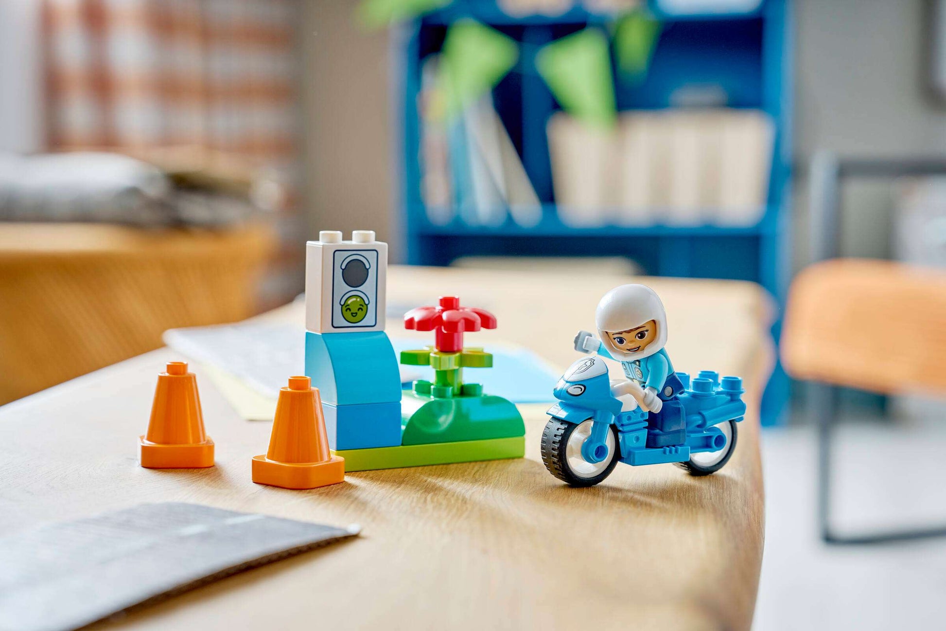 A LEGO® DUPLO® Blue Police Motorcycle by Legos - Toyhouse features a minifigure in a white helmet, traffic cones, flower, and small traffic light—ideal as an emergency vehicle or toddler learning toy.