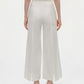 A person faces away, wearing Simkhai's Kallin Cropped Wide Leg Pant in white—high-waisted, heavy cotton trousers with front hem slits—paired with sandals, against a plain white background.