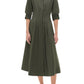 A woman wears the Simkhai Signature Jazz Dress—an olive green, collared, button-down cotton poplin midi with elbow-length sleeves—and black sandals, standing against a plain white background.
