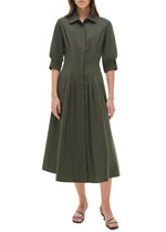 A woman wears the Simkhai Signature Jazz Dress—an olive green, collared, button-down cotton poplin midi with elbow-length sleeves—and black sandals, standing against a plain white background.