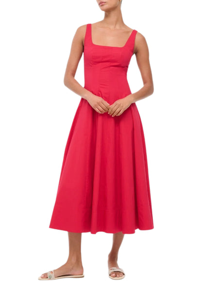 A woman wears the Staud Wells Dress, a sleeveless, square-neck, ankle-length red dress with a corset-style panel, fitted bodice for a flattering fit, flared skirt, and flat sandals.