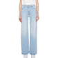 A person models The Hustler Roller Sneak high-rise, wide-leg jeans by Mother in light blue stretch denim with a white sleeveless top, shown from shoulders to feet against a plain background.