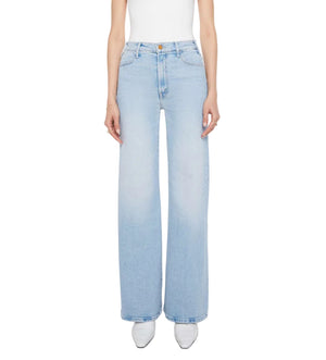 A person models The Hustler Roller Sneak high-rise, wide-leg jeans by Mother in light blue stretch denim with a white sleeveless top, shown from shoulders to feet against a plain background.