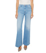 A model showcases Mother’s The Hustler Roller Sneak high-waisted, light blue stretch denim flare jeans with a white top, standing against a plain background; only the lower torso and legs are visible.