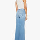 A woman is standing with her back to the camera against a white background, wearing a white sleeveless top and The Hustler Roller Sneak high-waisted stretch denim wide leg jeans by Mother in light blue.