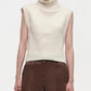 A person wears the Simkhai Maple Top, an ivory sleeveless turtleneck, styled with high-waisted brown leather pants for a structured silhouette, shown from shoulders to hips against a plain background.