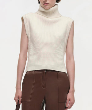 A person wears the Simkhai Maple Top, an ivory sleeveless turtleneck, styled with high-waisted brown leather pants for a structured silhouette, shown from shoulders to hips against a plain background.