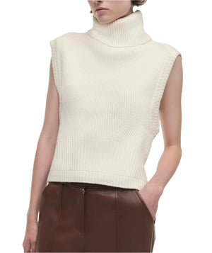 Wearing the Simkhai Maple Top, a person creates a minimalist look in a sleeveless turtleneck paired with high-waisted brown leather pants, one hand casually tucked in their pocket.