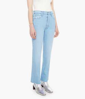 Person wearing The Tripper Flood Fray jeans by Mother in light blue denim, styled with a white sleeveless top and silver ankle boots, standing against a plain white background.