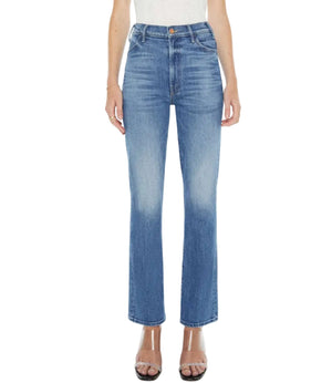 A person wears Mother’s The Hustler Flood mid-blue high-rise flare jeans in stretch denim, paired with a white top and clear-heeled sandals, shown from shoulders to feet against a white background.