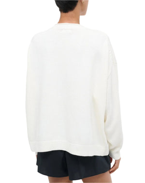A person is seen from the back wearing a loose Staud Giada Sweater in white with black shorts. This lightweight summer sweater features a subtle sardines jacquard pattern, shown against a plain background.