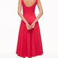 A woman, her back to the camera, wears the Staud Wells Dress—a bright red, ankle-length cotton poplin style with a flattering corset-inspired panel. Her hands are clasped behind her back and she's wearing flat sandals.