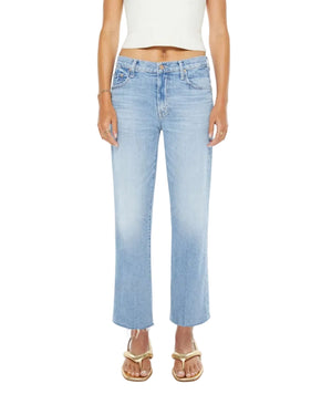 A person stands against a plain white background wearing a white crop top, Mother’s Mid Rise Rambler Zip Ankle Fray jeans with a wide straight leg and frayed hem, and gold sandals.