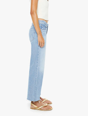 A person wearing a white sleeveless top, tan sandals, and Mother’s Mid Rise Rambler Zip Ankle Fray jeans stands in profile against a plain white background.