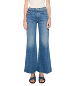 A person wearing Mother’s Tomcat Roller Sneak high-waisted, wide-leg vintage-inspired blue jeans and dark sandals, standing against a white background.