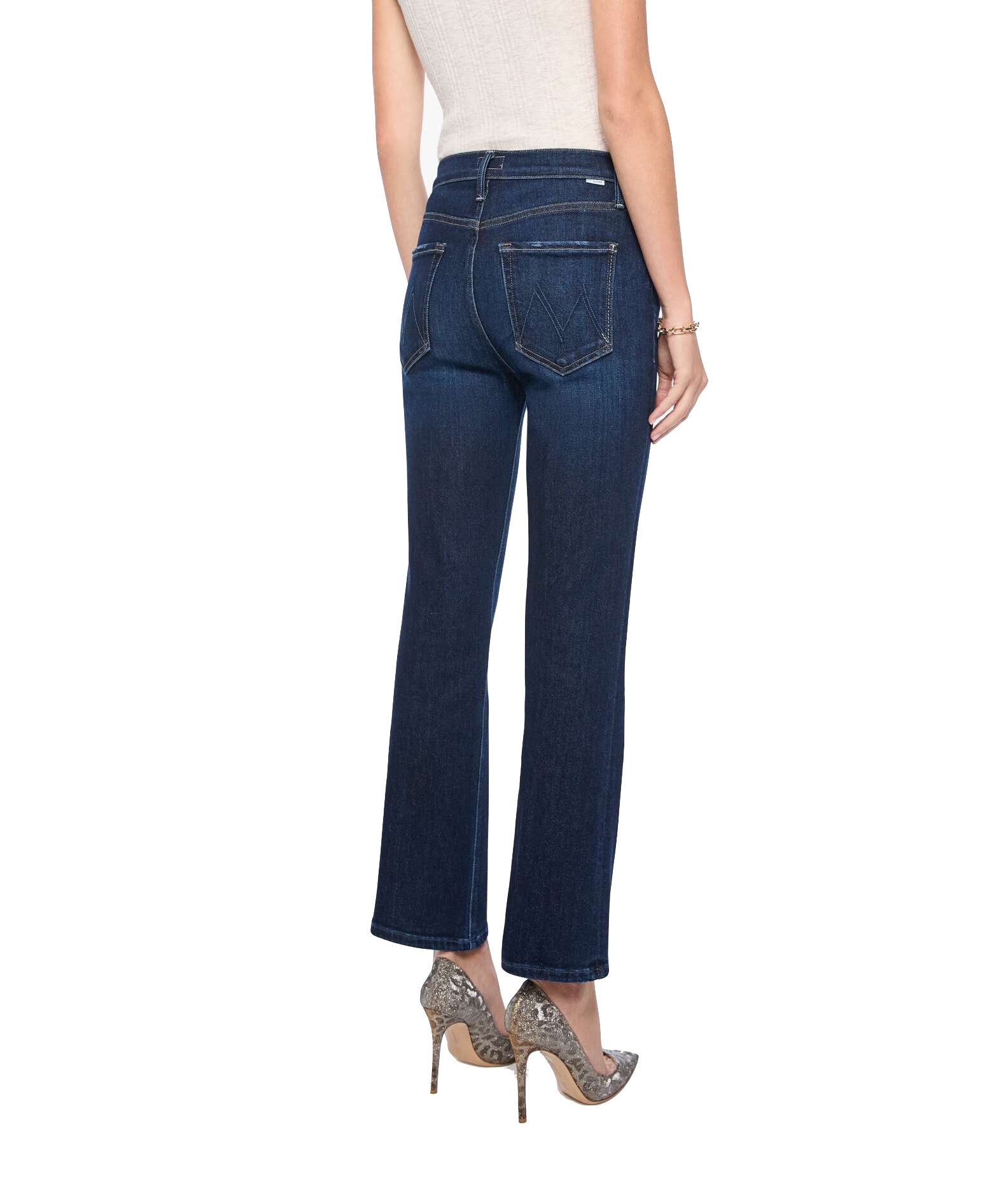 A person is shown from the back on a white background wearing the Mother Tripper Flood high-rise flare bootcut jeans in dark blue stretch cotton blend, paired with a white sleeveless top and snakeskin high heels.