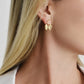 A woman with straight blonde hair wears Anabel Aram's Butterfly with Enamel Flower Earring, crafted in 18k gold. She's dressed in a white collared shirt, with only her ear and a portion of her jaw and neck visible.