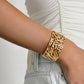 A person wears a white ruched top and light denim jeans, accessorized with the Anabel Aram Palm Leaves Cuff—an 18k gold-dipped bracelet styled like palm fronds.