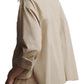 Wearing a TWP Day After Top in beige, with relaxed-fit cotton poplin pants and their left hand in the pocket, they slightly turn their head against a plain white background.