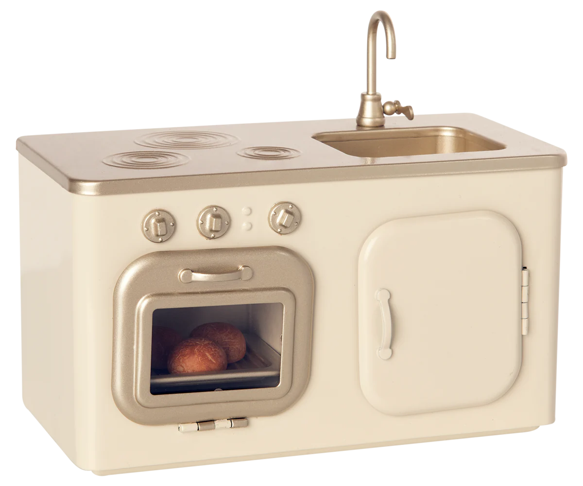 The Maileg Miniature Kitchen is a compact set featuring a beige and gold stove, oven with baked buns, sink, and cupboard.