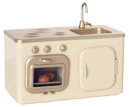 The Maileg Miniature Kitchen is a compact set featuring a beige and gold stove, oven with baked buns, sink, and cupboard.