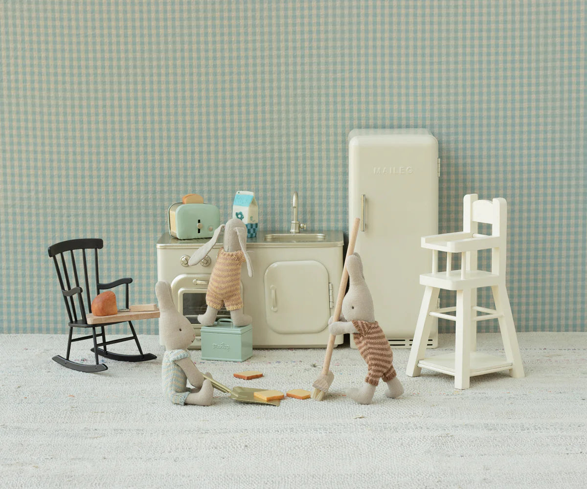 Three micro bunnies play in a vintage kitchen—one mops, another holds a sponge, and the third stands by the Maileg High Chair - Micro among charming miniature toy furniture.