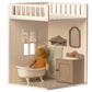 The Maileg House of Miniature Bathroom showcases a delightful scene with a charming teddy bear lounging in a classic clawfoot bathtub, complemented by elegant dollhouse furniture such as a sink with mirror, a side towel, and a delicate lace curtain framing the window.