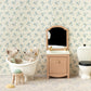 Two Maileg plush animals sit in a white bathtub next to the Sink Dresser, Mouse - Powder in a miniature mouse house bathroom decorated with floral wallpaper, featuring a mirror and toilet.