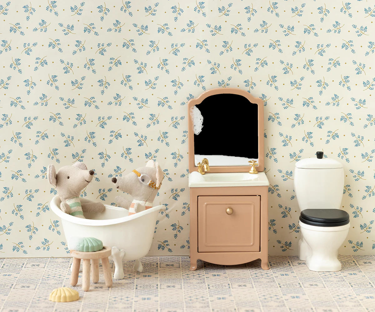 Two Maileg plush animals sit in a white bathtub next to the Sink Dresser, Mouse - Powder in a miniature mouse house bathroom decorated with floral wallpaper, featuring a mirror and toilet.