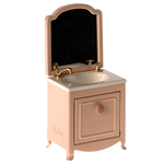 The Maileg Sink Dresser, Mouse - Powder is a small pink vanity with a mirror, gold faucet, and cabinet door below the bathroom sink.