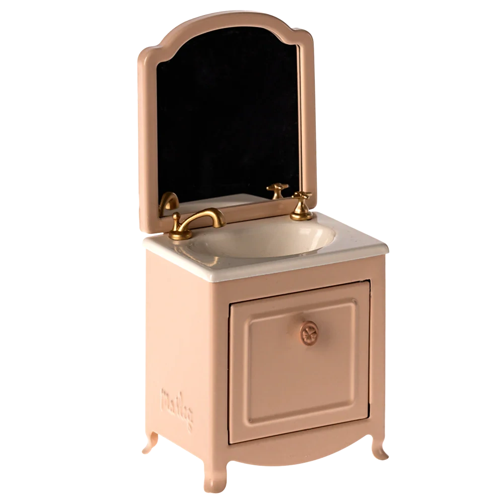 The Maileg Sink Dresser, Mouse - Powder is a small pink vanity with a mirror, gold faucet, and cabinet door below the bathroom sink.